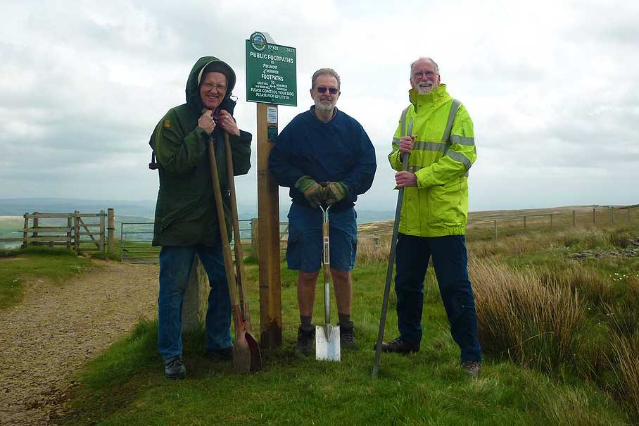 Three volunteers with digging tools next to the footpath sign they've just planted.
