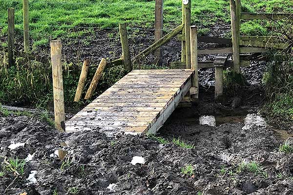 A wide muddy ditch next to a stile.