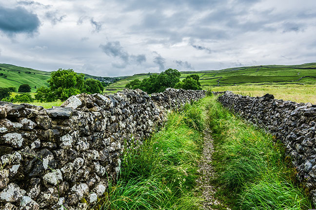 Looking along a long footpath at Malham Cove with stone walls on each side